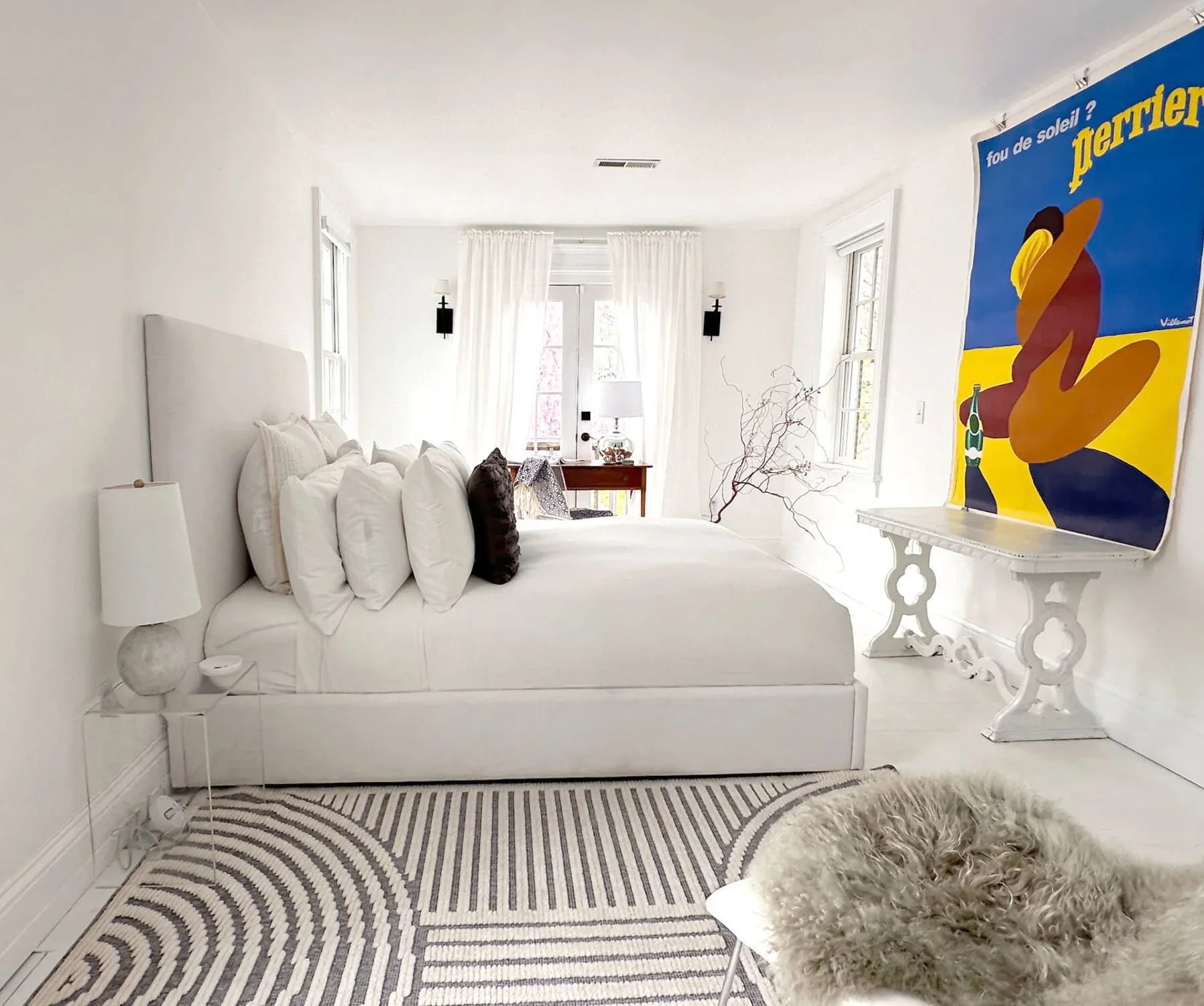 Guest bedroom with a plush made bed, layered linens, and vintage art above a painted headboard wall