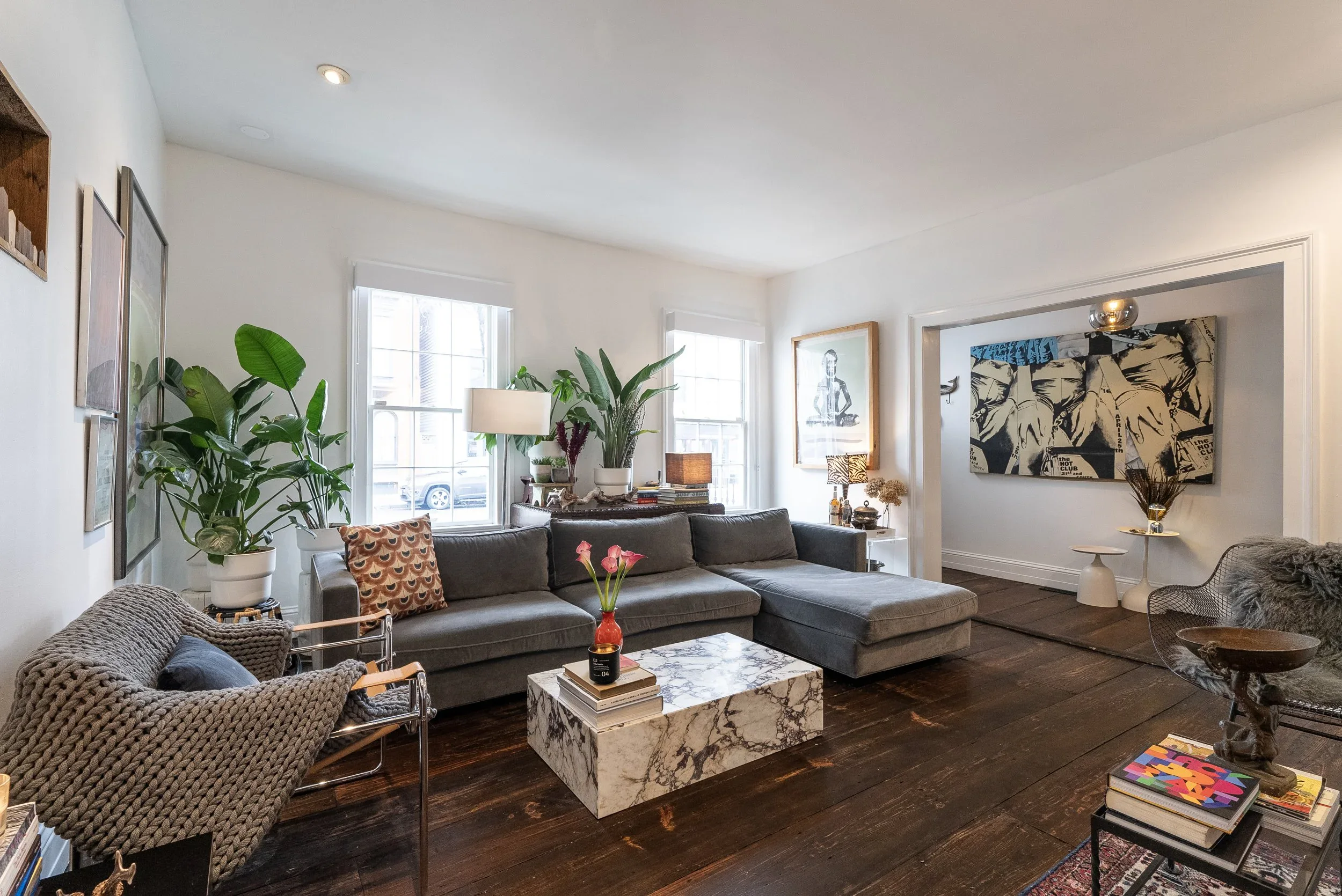 Cinematic sunlit living room with layered vintage furniture, collected art, and tall historic windows